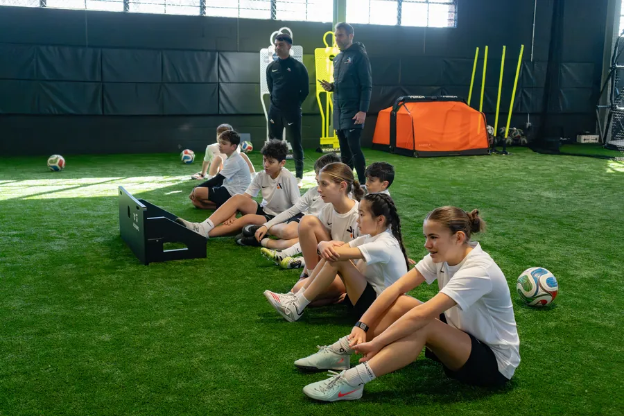 Players sitting on the turf listening to two coaches